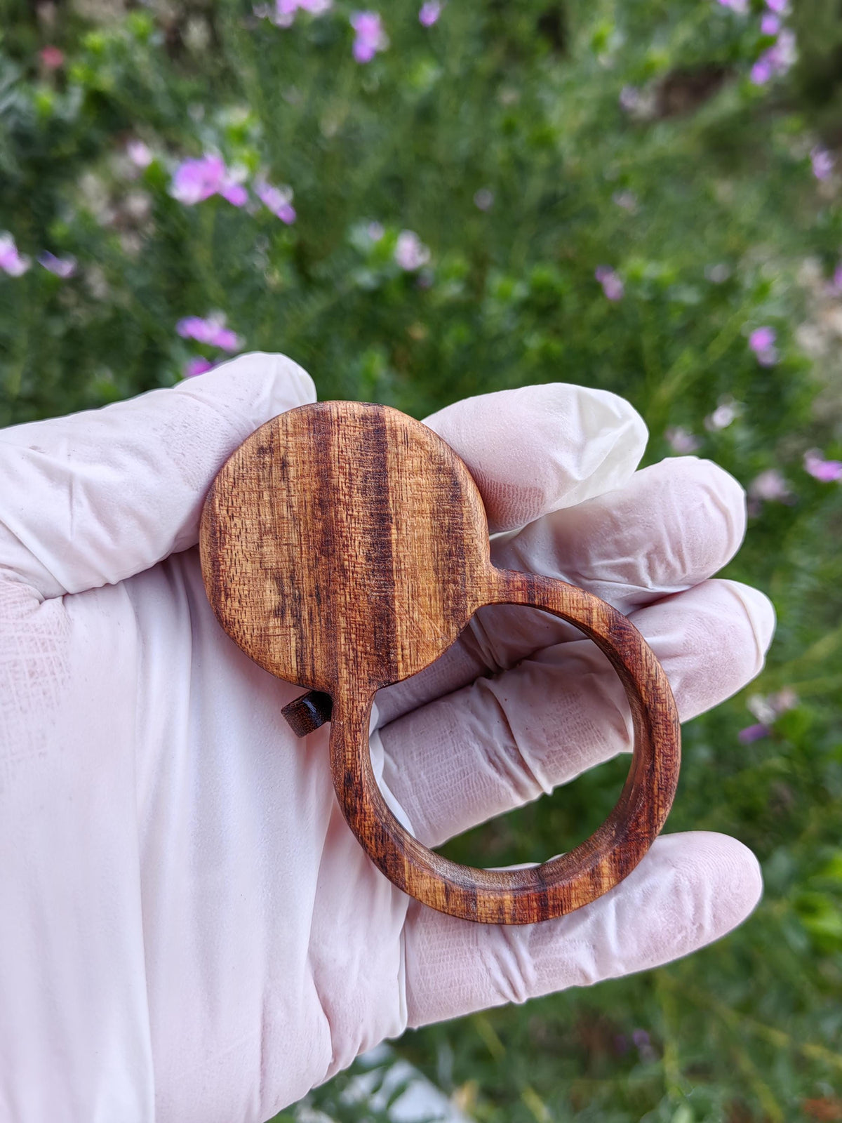 Wooden magnifying glass pendant with hidden AirTag compartment for tracking device.