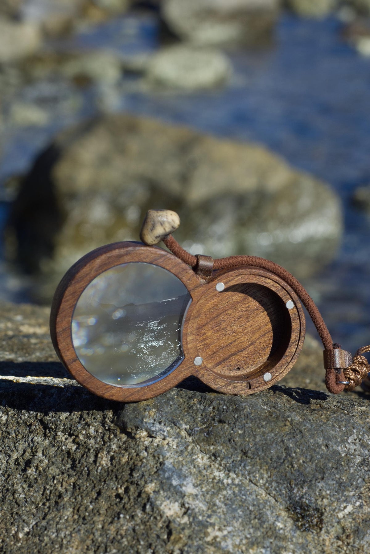 Wooden magnifying glass pendant with hidden AirTag compartment for tracking device.